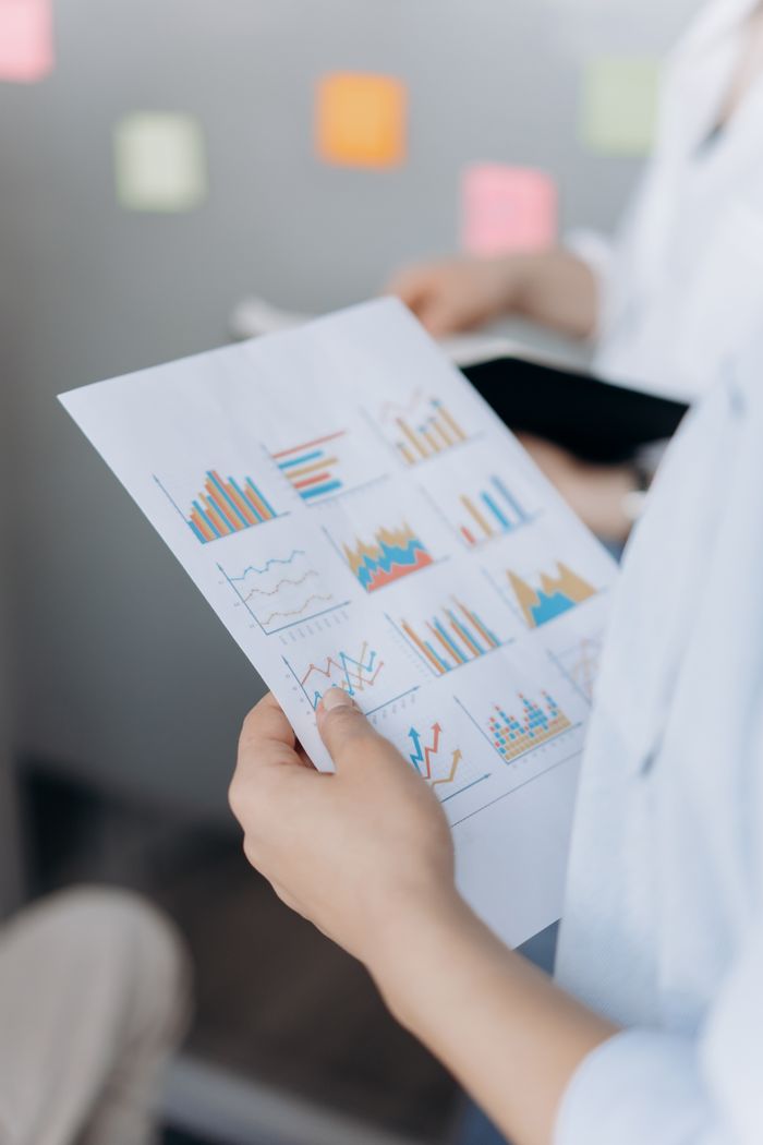 who-we-are Close-up of hands holding paper with various business graphs in an office setting.