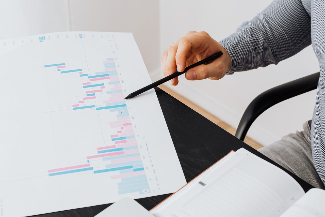 team-01 Close-up of a person analyzing a colorful graph chart with a pen in a modern office setting.